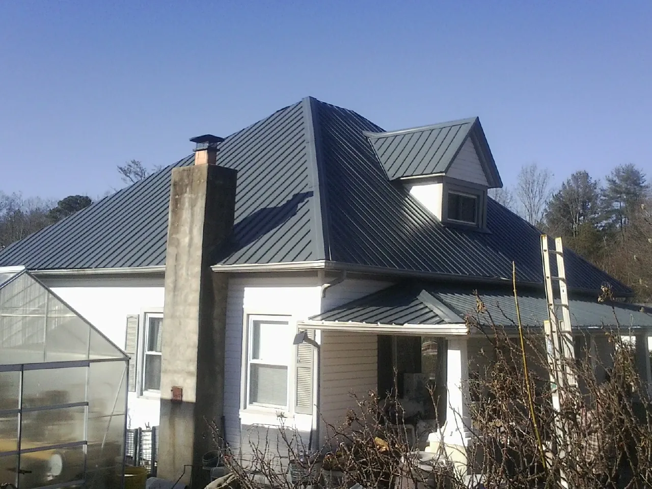 Dark blue standing seam metal roof on a white farmhouse with dormer — Slate & Tile Roof Repair by Roofing Brothers in Manning