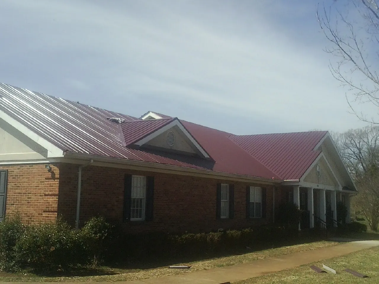 Red metal roof with gabled entries on a long brick building, from a Hail Damage Roof Repair job in Manning