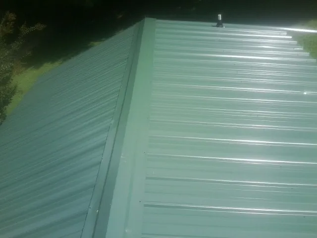 New green metal panels meeting at the ridge of a roof — Flat Roof Repair work by our crew in Manning