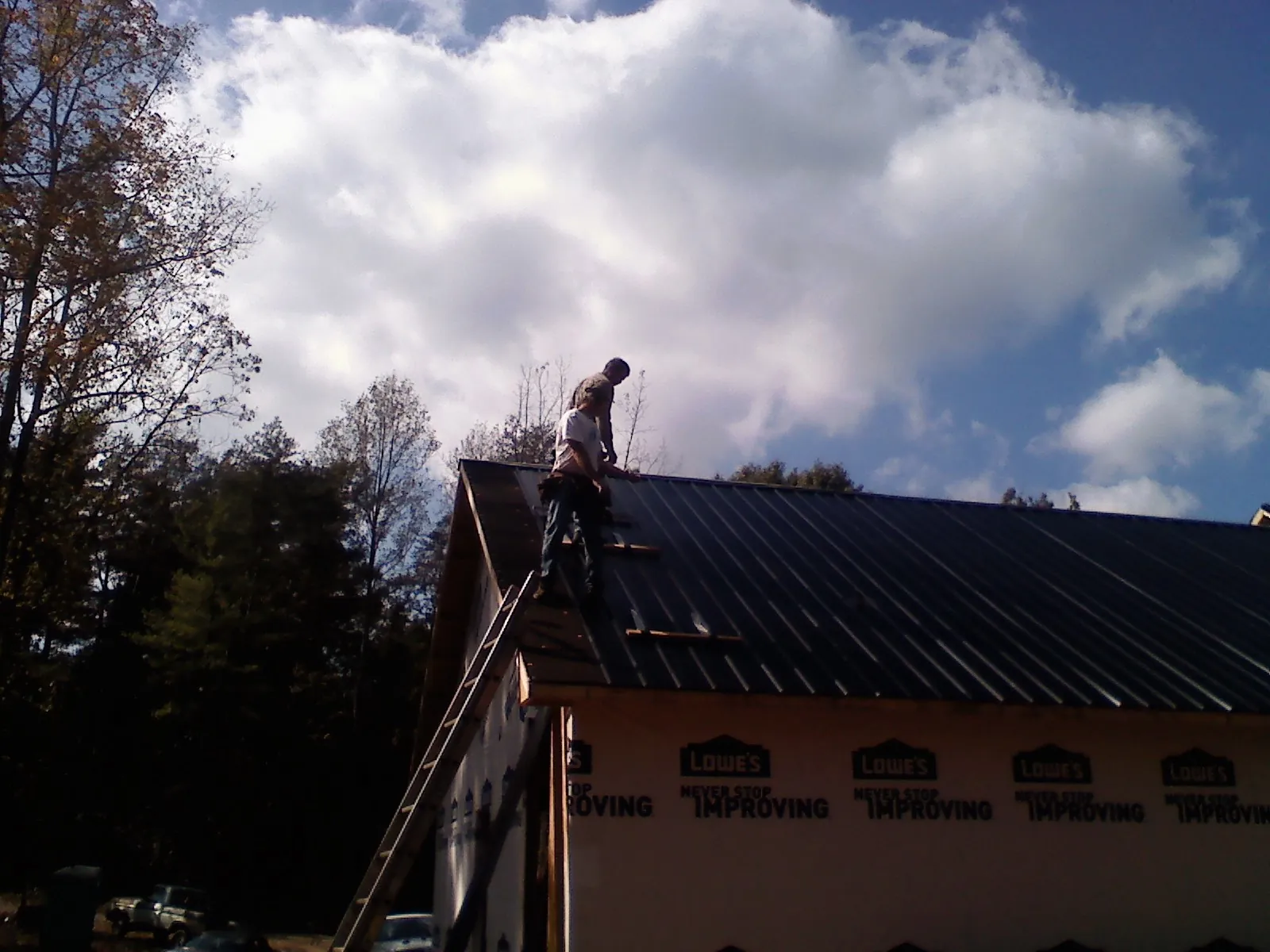 Roofer fastening dark metal panels high against a cloudy sky, from a Roof Inspection job in Manning