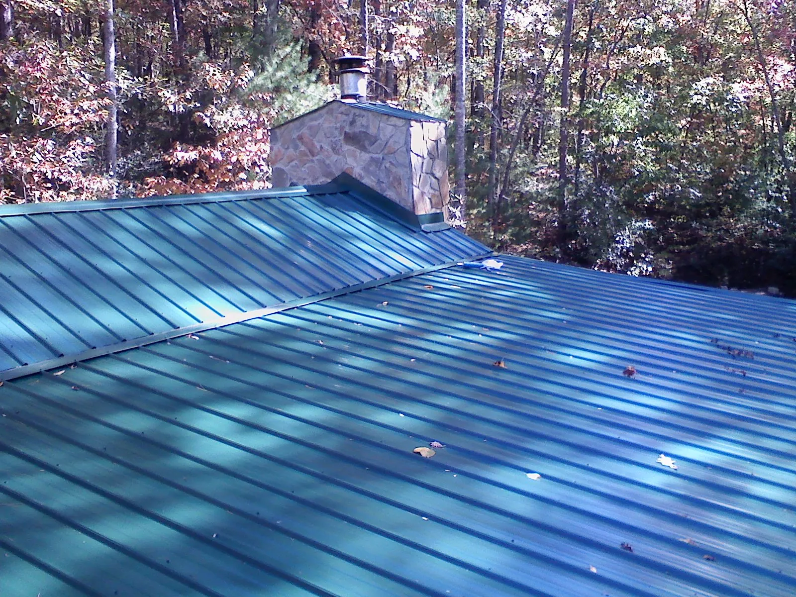 New green metal roof and stone chimney surrounded by autumn woods in Manning